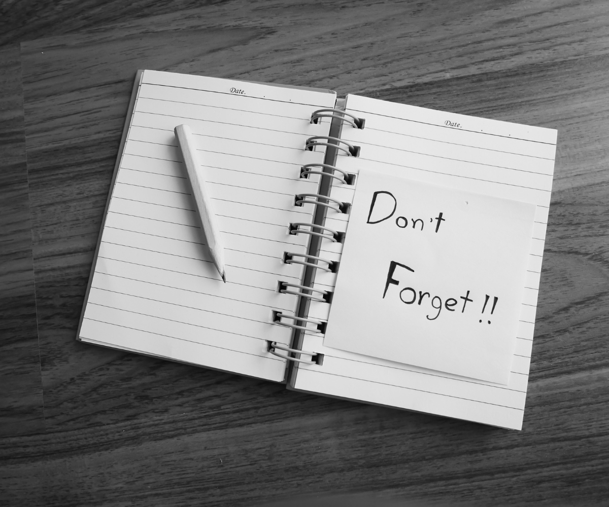 Notebook with a reminder note that says "Don't Forget," representing the importance of regularly reviewing and improving advertising campaigns rather than setting them and forgetting them.