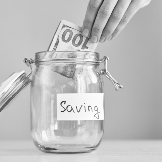 Hand placing money into a savings jar, representing business owners trying to save advertising money by improving their current marketing before increasing their advertising budget and getting better results.