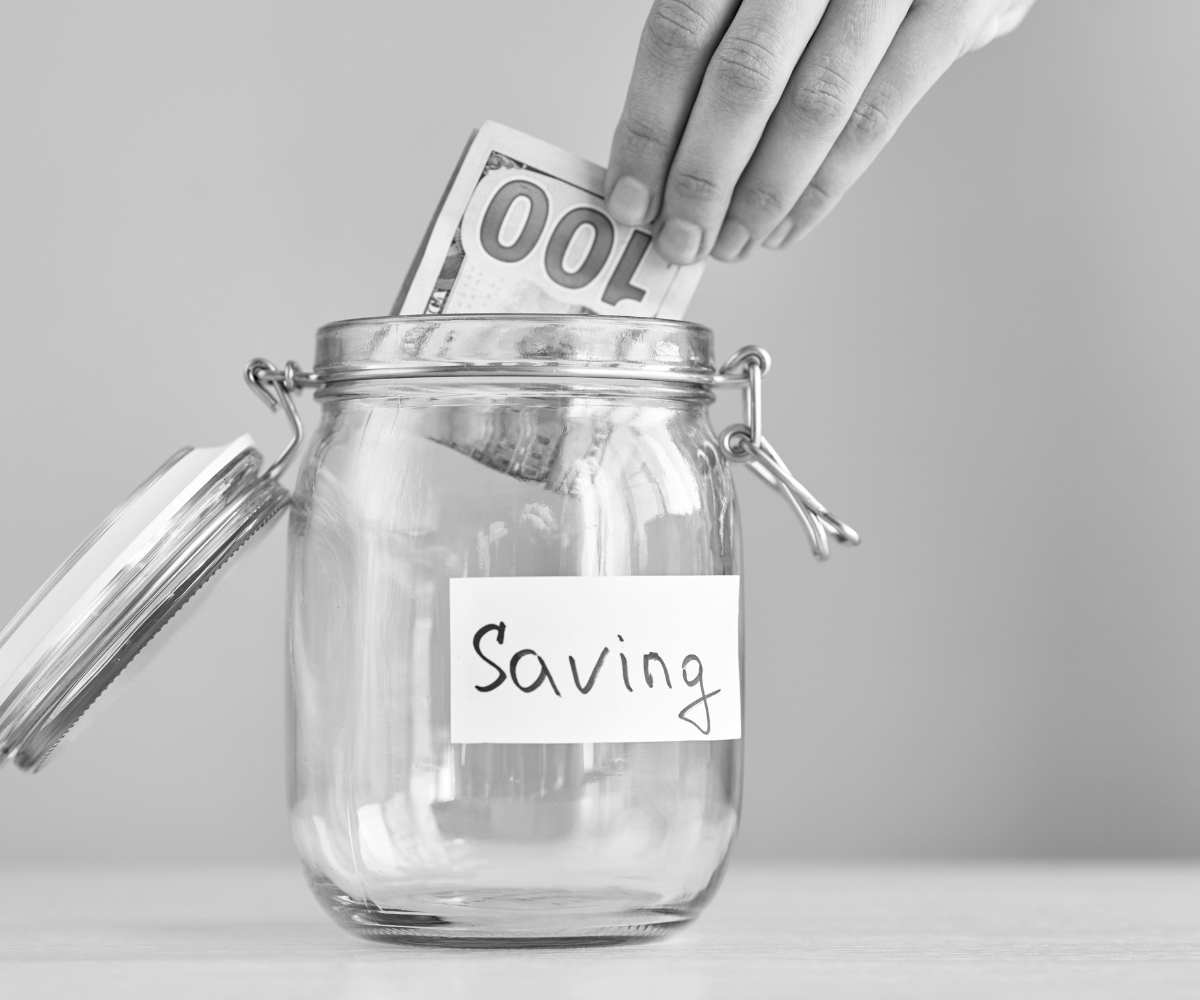 Hand placing money into a savings jar, representing business owners trying to save advertising money by improving their current marketing before increasing their advertising budget and getting better results.